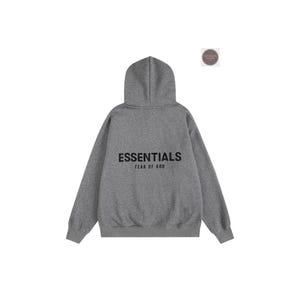 K&ouml;nnte beinhalten: Ein grauer Kapuzenpullover mit dem schwarzen Aufdruck "ESSENTIALS" auf dem R&uuml;cken und "FEAR OF GOD" darunter. Der Pullover hat eine Kapuze mit Kordelzug und lange &Auml;rmel. Der Hintergrund ist wei&szlig;.