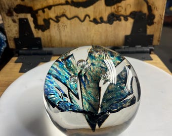 May include: A clear glass paperweight with blue, green, and gold swirls and air bubbles inside.