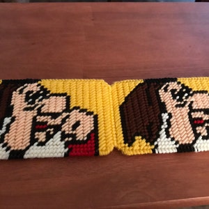 May include: Two yellow and brown crocheted coasters with a cartoon image of a woman with brown hair and a red and white shirt. The coasters are made of plastic canvas.