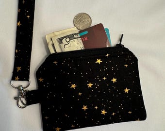 May include: A small black zippered pouch with a gold star pattern and a black and white star patterned strap. The pouch is open and contains cash, a credit card, and a coin.
