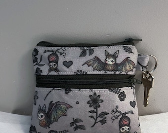 May include: A small gray zippered pouch with a double zipper. The pouch has a black and white print of bats and flowers. A key is attached to the zipper pull.