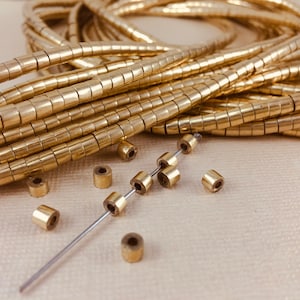 May include: A close-up of a pile of gold-colored metal beads. The beads are small and round, and they are arranged in a random pattern. Some of the beads are strung on a thin wire.