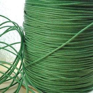 May include: A spool of green waxed cotton cord. The cord is wound tightly around the spool, creating a smooth, even surface.