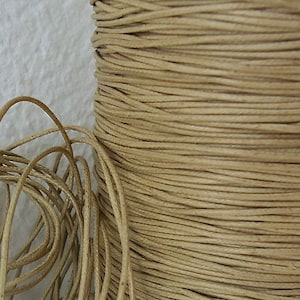May include: A spool of natural beige waxed cotton cord. The cord is wound tightly around the spool, creating a smooth, even surface.