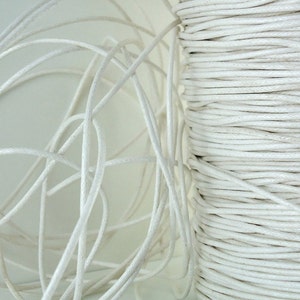 May include: A close-up of a spool of white cotton cord. The cord is tightly wound and has a smooth, matte finish.