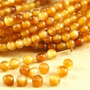 May include: Close-up of strands of amber-colored beads. The beads are round and have a polished, glossy finish. Some beads are strung on a thin wire, while others are loose. The color varies from light yellow to deep brown.