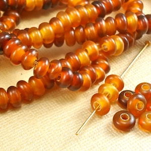 May include: A strand of amber-colored glass beads, with a few loose beads scattered nearby. The beads are round and have a slightly irregular shape. They are a warm, honey-like color.