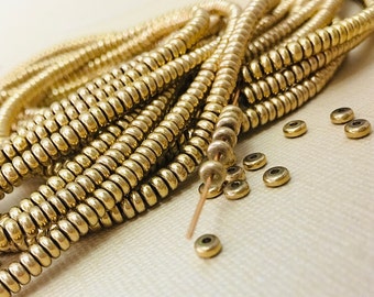 May include: A strand of gold-colored metal beads, each bead is a small ring with a slightly raised edge. The beads are arranged in a coil shape, and there are several loose beads scattered around the coil.