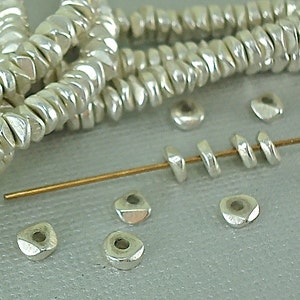 May include: Silver metal beads in a variety of shapes and sizes. The beads are arranged in a pile and on a wire. The beads are all silver in color and have a shiny finish.
