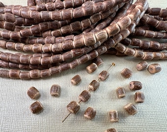 May include: Strands of brown, barrel-shaped beads with a light-colored, textured pattern. Some beads are strung on a gold-colored pin, while others are loose. The beads are likely for jewelry making or crafts.