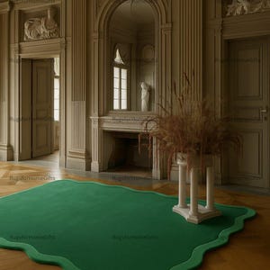 Op de afbeelding: Een groen, organisch gevormd tapijt met een donkerdere groene rand op een houten vloer. De kamer heeft klassieke architectonische details, waaronder zuilen, lijsten en sculpturen. Een decoratief bloemstuk staat op een witte sokkel.