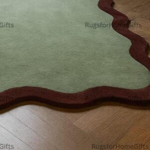 May include: A sage green rug with a wavy, dark red border. The rug is on a wooden floor. The text "RugsforHomegifts" is visible in the image.