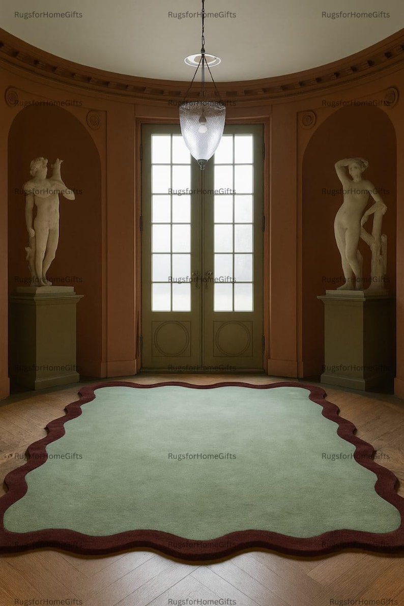 May include: An interior scene showing a light green rug with a dark red, wavy edge. The rug is in a room with statues, a large door, and a hanging light. The walls are a warm peach colour, and the floor is wooden.