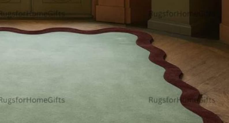 May include: A pale green rug with a dark red, wavy border. The rug has a rectangular shape and a soft, plush texture. The design is simple and elegant, suitable for a living room or bedroom.