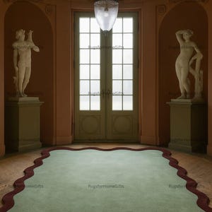 May include: An interior scene showing a light green rug with a dark red, wavy edge. The rug is in a room with statues, a large door, and a hanging light. The walls are a warm peach colour, and the floor is wooden.