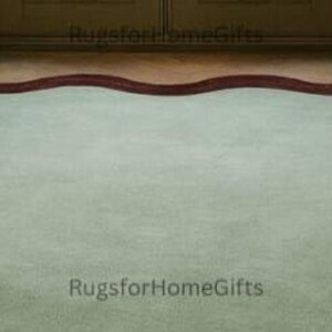 May include: A large, pale green rug with a dark red, wavy border. The rug is placed on a wooden floor, with a doorway in the background. The rug's distinctive shape and colour scheme create a striking visual contrast.