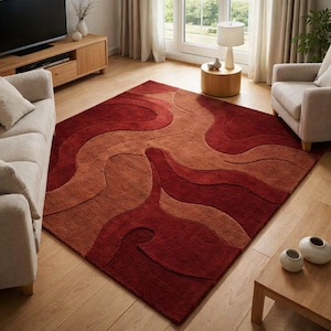 Könnte beinhalten: Ein rechteckiger Teppich mit einem fließenden, abstrakten Design in Rot- und Beigetönen. Der Teppich liegt auf einem Holzboden in einem Wohnzimmer, mit Möbeln im Hintergrund.