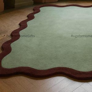 May include: A large, sage green rug with a wavy, dark red border. The rug is placed on a hardwood floor with a herringbone pattern. The rug's unique shape and colour palette add a modern touch to the room.