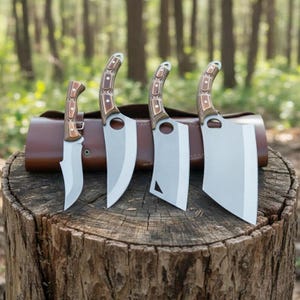 May include: A set of four stainless steel cleavers and knives with wooden handles, displayed on a tree stump. The blades vary in size and shape, with a brown leather sheath in the background. The knives are designed for kitchen use.