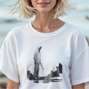 May include: White t-shirt featuring a black and white illustration of a hooded figure playing golf. The text "I LOVE GOLF" is printed on the golf club. The shirt is a casual, comfortable style.