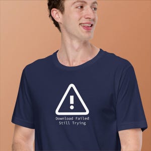 May include: A navy blue t-shirt with a white warning triangle containing an exclamation mark and the text "Download Failed Still Trying". The shirt is made of a soft material.