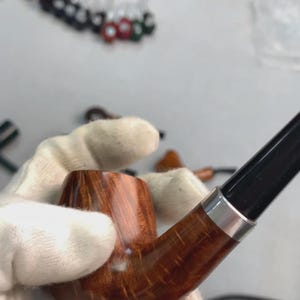 Könnte beinhalten: Nahaufnahme einer Tabakpfeife aus Holz mit einer dunkelbraunen Pfeifenkopf und einem schwarzen Mundstück. Die Pfeife hat ein silbernes Band, wo Pfeifenkopf und Mundstück verbunden sind. Die Holzmaserung ist sichtbar.