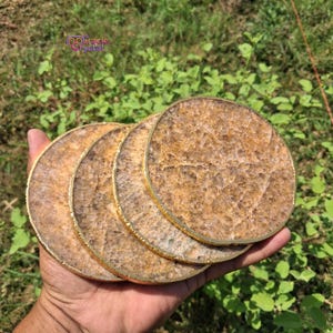 Puede incluir: Un juego de cuatro posavasos redondos con un aspecto natural y texturizado. Cada posavasos tiene un borde de metal dorado. Los posavasos se sostienen en una mano sobre un fondo de follaje verde. El texto "miracle crystal" es visible.