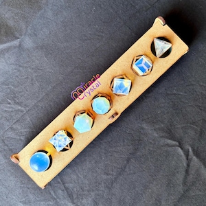 May include: A wooden display case holding six opalescent crystal shapes. The crystals include a sphere, a square, a hexagon, a cube, a pyramid, and a diamond shape. The case has the text "Miracle Crystal" in a purple script.