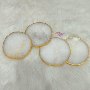 Op de afbeelding: Vier ronde onderzetters van witte agaat met goudkleurige randen. De onderzetters hebben natuurlijke kleur- en textuurvariaties. Ze liggen op een witte, zachte ondergrond.