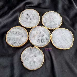 May include: Six round coasters with a natural, translucent white stone center and a gold-colored, irregular edge. The coasters are arranged in a circular pattern on a dark, textured surface. The "Miracle Crystal" logo is visible in the lower right corner.