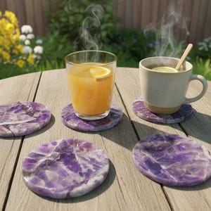 May include: A wooden table with a glass of orange juice and a mug of tea, both with lemon slices. The drinks sit on round, purple amethyst coasters. Steam rises from the drinks. Yellow flowers are in the background.