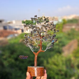 May include: A handcrafted crystal tree sculpture with a brown trunk and branches, adorned with dark gray and blue-green crystals. The tree sits on a wooden base and features the text "miracle crystal".