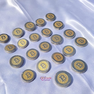 Può includere: Una collezione di monete Bitcoin argentate con simboli "B" dorati, disposte su una superficie bianca e serica. Le monete sono rotonde e hanno una lucentezza metallica, creando un contrasto con lo sfondo morbido.