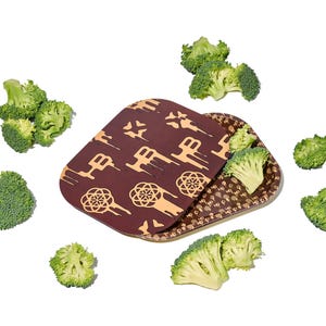 Peut inclure: Un plateau de service marron avec un motif géométrique, ouvert pour révéler un intérieur à motifs. Des fleurons de brocoli sont dispersés autour du plateau, certains étant placés à l'intérieur. Le plateau est rectangulaire avec des coins arrondis.
