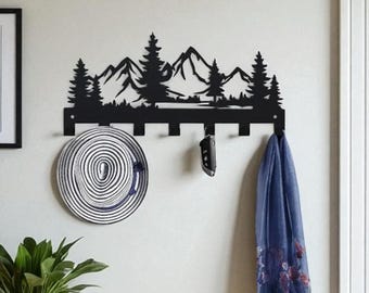 May include: A black metal wall-mounted coat rack featuring a mountain and tree silhouette design. A framed print with the word "WELCOME" hangs on the wall. A bench with a woven basket and a potted plant complete the entryway decor.
