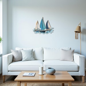 Könnte beinhalten: Metall-Wandkunst mit drei Segelbooten mit blauen und weißen Segeln, vor dem Hintergrund stilisierter blauer Wellen. Die Segelboote sind in Blau- und Weißtönen gehalten und schaffen ein maritimes Thema. Das Kunstwerk ist an einer weißen Wand befestigt.