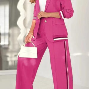Puede incluir: Un traje pantal&oacute;n fucsia vibrante con blazer y pantal&oacute;n de pernera ancha. La blazer tiene un solo bot&oacute;n, bolsillos y detalles de rayas en las mangas y el bolsillo. El pantal&oacute;n tiene una raya vertical. Tambi&eacute;n se ve un bolso blanco.