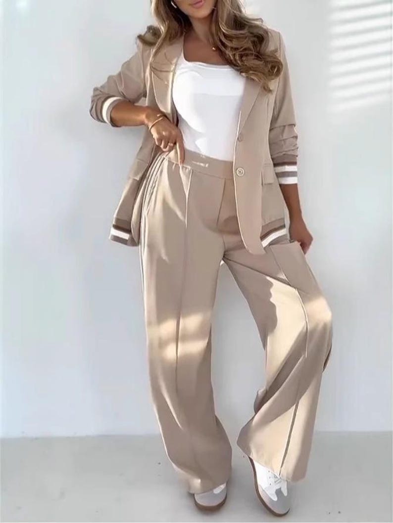 Puede incluir: Un traje pantal&oacute;n beige compuesto por una blazer y pantalones de pernera ancha. La blazer tiene un cierre de un solo bot&oacute;n y detalles a rayas en las mangas. Se lleva una camiseta blanca debajo. El conjunto se combina con zapatillas blancas y grises.