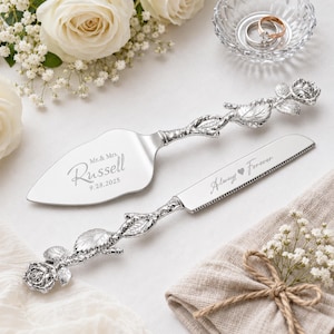 May include: A silver cake server and knife set with handles shaped like rose stems and blossoms. The server is engraved with Mr. & Mrs. Russell 9.28.2025 and the knife is engraved with Always Forever. The metal blades have a polished finish.