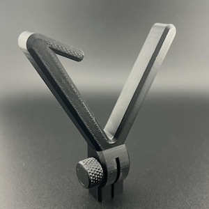 Könnte beinhalten: Ein schwarzer, 3D-gedruckter Kamerahalter mit V-förmigem Design. Die Halterung verfügt über einen strukturierten Knopf zur Einstellung und einen Schlitz zur Befestigung. Das Objekt besteht aus schwarzem Kunststoff und ist für eine Kamera konzipiert.