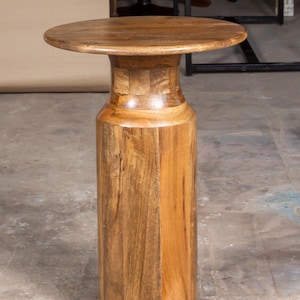 Puede incluir: Una mesa auxiliar de madera maciza con una tapa redonda y una base cilíndrica. La mesa es de madera de color marrón claro y tiene un acabado natural. La mesa mide aproximadamente 61 cm de altura.