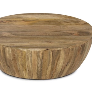 May include: A round, low coffee table made of light brown wood. The table has a solid, curved base and a flat top. The wood grain is visible, giving the table a natural, rustic appearance. The table is suitable for a living room or lounge area.