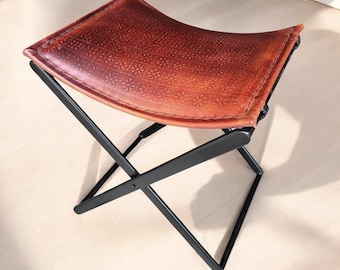 Taburete plegable de piel marroquí – Asiento tipo puf repujado a mano con estructura en X de hierro negro