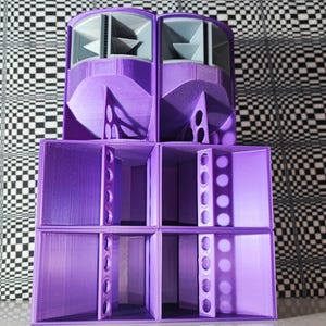 May include: A stack of purple speaker cabinets with a geometric design. The speakers are arranged in a tiered configuration, with two rounded top units and four rectangular lower units. The background features a black and white checkered pattern.