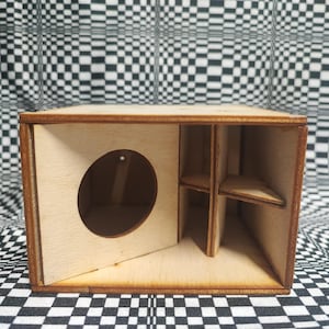 May include: A small, unfinished wooden box with a circular opening on the front panel. The box has internal dividers creating separate compartments. The wood has a light color with darker brown edges.