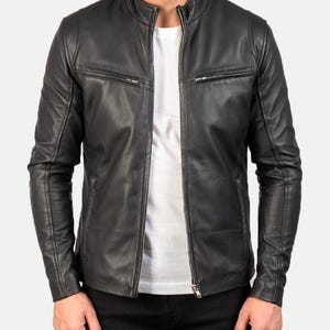 May include: Black leather jacket with a stand-up collar and a front zipper closure. The jacket has two zippered chest pockets and long sleeves. The model is wearing a white t-shirt underneath.
