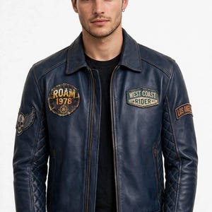 Könnte beinhalten: Eine marineblaue Lederjacke mit klassischem Kragen, Frontreißverschluss und gesteppten Details an den unteren Ärmeln und am Saum. Die Jacke ist mit Aufnähern versehen, die den Text ROAM 1978, WEST COAST RIDER und LOS ANGELES tragen.
