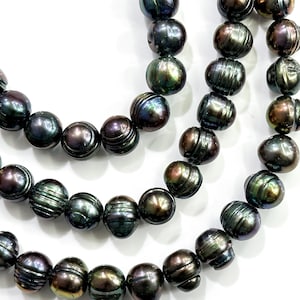 Pode incluir: Close-up de três fios de pérolas escuras e iridescentes. As pérolas têm um brilho profundo e lustroso com toques de verde, roxo e bronze. As contas são redondas com cristas sutis, criando uma aparência texturizada. O fundo é branco liso.