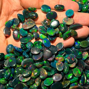 May include: A selection of polished black opal gemstones, displaying flashes of green, blue, and red. The opals are in various shapes and sizes, highlighting their unique colour play. These gemstones are suitable for jewellery making.