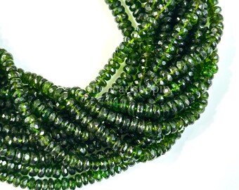 May include: Close-up of a collection of faceted, dark green beads. The beads are strung together, forming multiple strands. The beads have a reflective, polished surface, and are arranged against a white background. The overall theme is jewelry and gemstones.